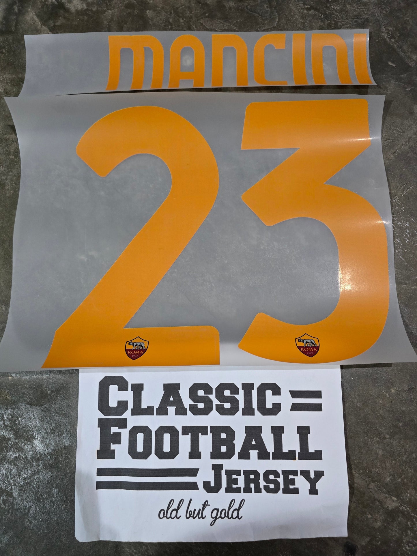 Two printed items on a textured surface, one with '23' and 'Mancini', the other with 'Classic Football Jersey'.